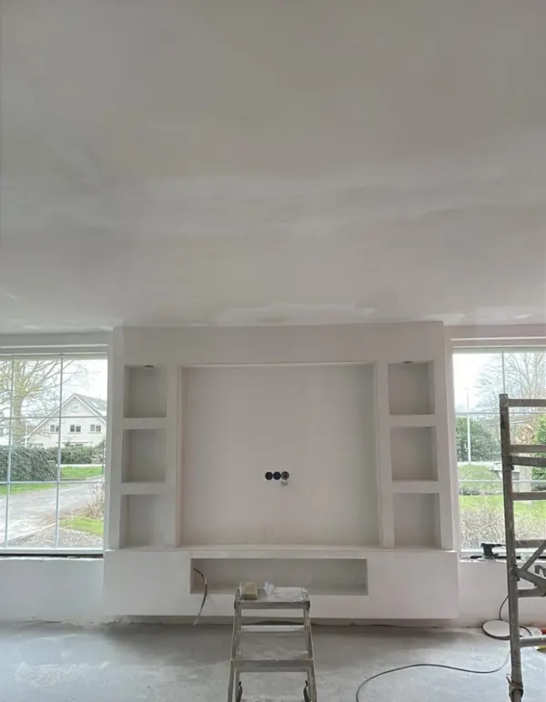 Woonkamer met vers gestuct plafond en een witte TV-wand met nissen