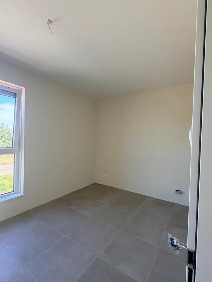 Slaapkamer met raam en strak afgewerkte lichte wanden en plafond